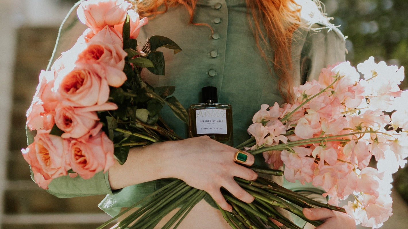 Person holding a bouquet of pink flowers with a bottle of perfume in the center.